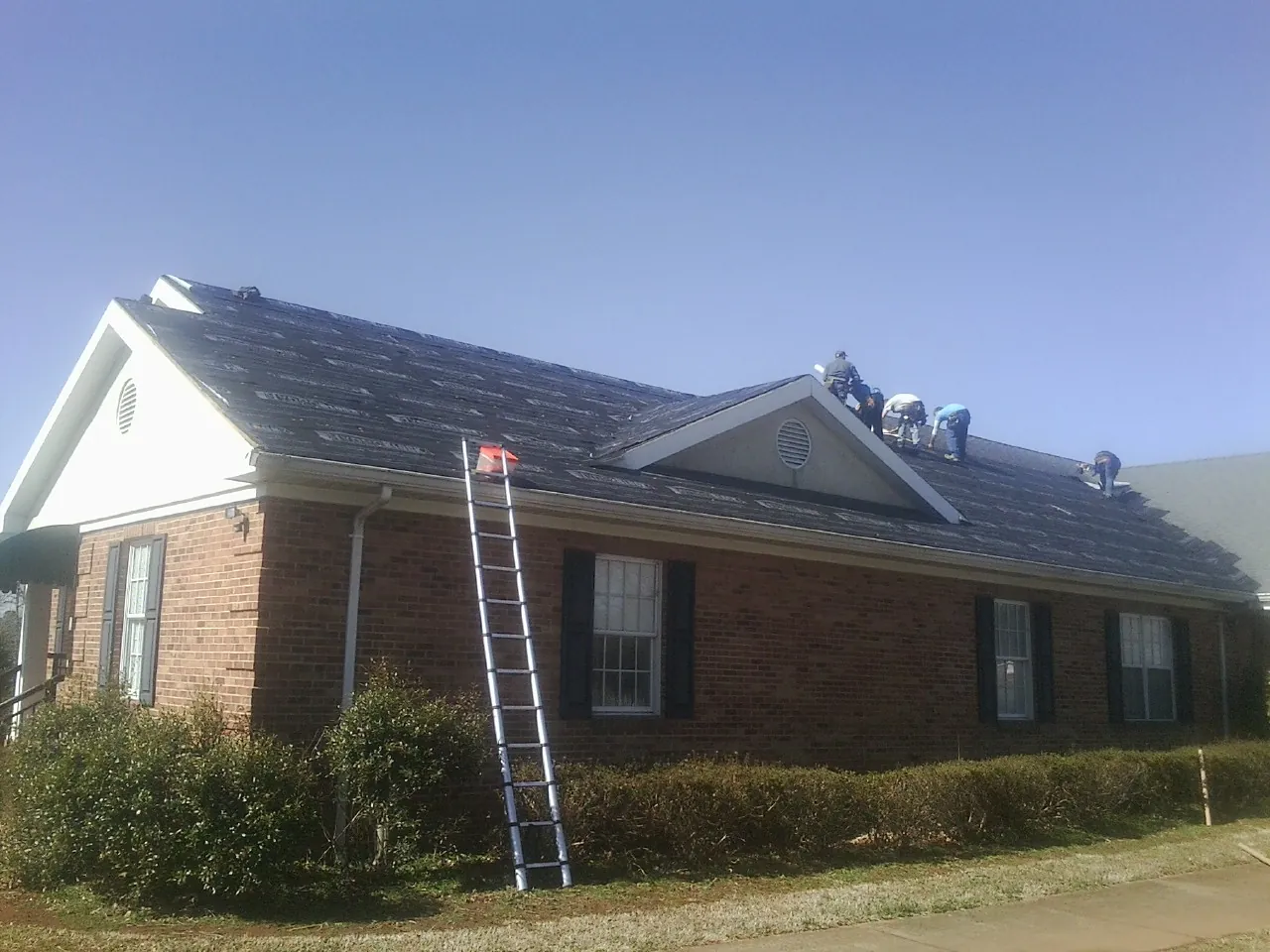 Crew tearing shingles off a brick ranch roof with a ladder set — Emergency Roof Repair work by our crew in Olema