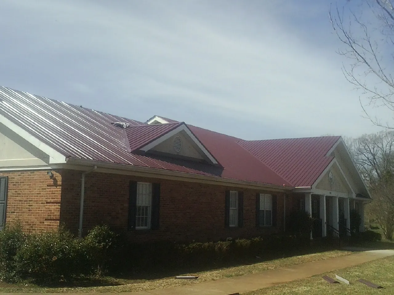 Red metal roof with gabled entries on a long brick building, from a Hail Damage Roof Repair job in Olema