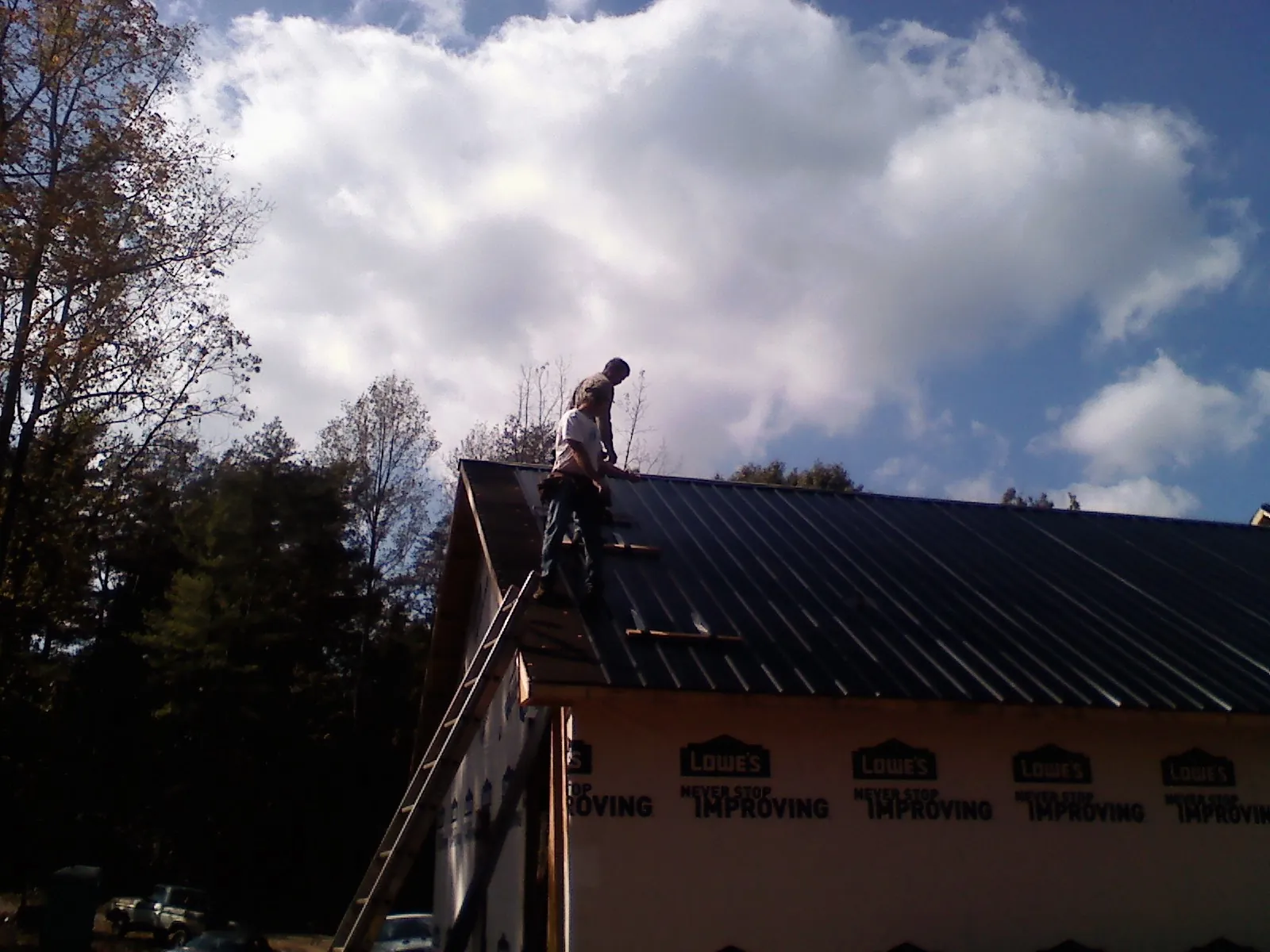 Roofer fastening dark metal panels high against a cloudy sky, from a Roof Inspection job in Olema