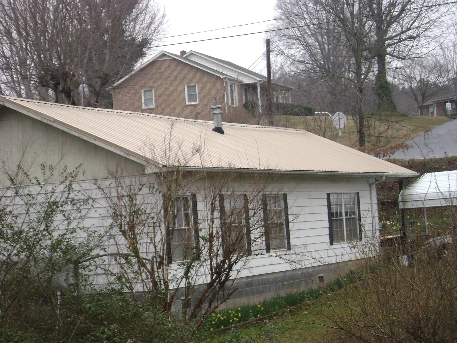 Tan metal roof on a white sided house set into a hillside — Commercial Roofing by Roofing Brothers in Olema